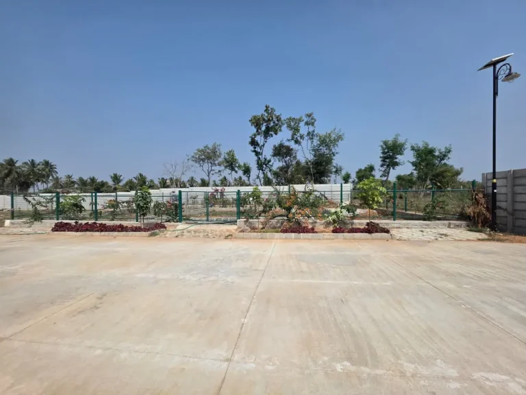 Landscaped residential property with flowering plants, green fencing, paved grounds, and solar-powered street lighting.